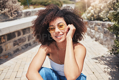 Portrait of young trendy beautiful mixed race woman with an afro smiling and posing alone outside. Hispanic woman wearing sunglasses and feeling happy. Fashionable African American woman in the city
