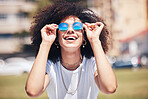 Cool, happy hispanic woman wearing sunglasses outside. Cheerful young woman with a curly afro wearing trendy, stylish sunglasses while enjoying a summer day at the park outside. Young woman laughing