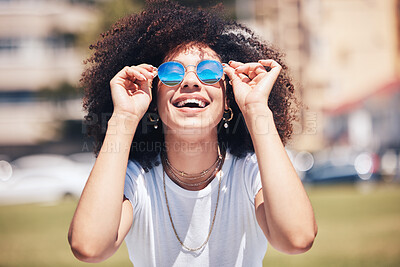 Cool, happy hispanic woman wearing sunglasses outside. Cheerful young woman with a curly afro wearing trendy, stylish sunglasses while enjoying a summer day at the park outside. Young woman laughing