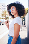 Young stylish mixed race woman with curly natural afro hair wearing trendy glasses outside. One female only looking carefree, cool and confident. Happy fashionable hispanic woman standing in the city