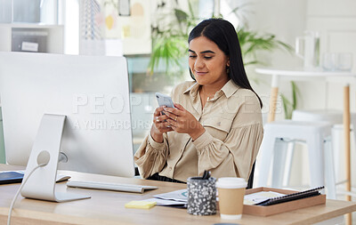 Young indian businesswoman sitting alone in an office and browsing the internet on a cellphone. Ambitious mixed race creative professional networking with clients while using technology in a workspace