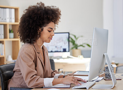 One young busy African American woman using a desktop while sitting at a desk in her office job. Black woman with an afro typing an email at her job. Mixed race woman focused on typing on a keyboard
