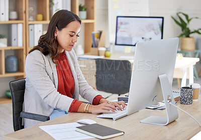 Young confident asian business woman sitting alone in an office and browsing the internet on a computer. Ambitious creative professional networking and emailing clients at a desk. Entrepreneur at work