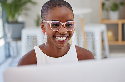 Young african american businesswoman wearing glasses, smiling and working on a computer in an office. One female only browsing online while planning on a desktop pc at her desk. Confident hard working black female entrepreneur completing deadlines and sen