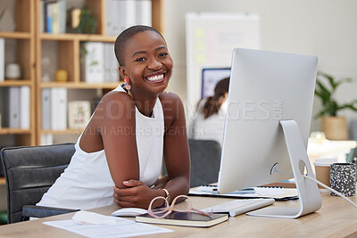 Cheerful young african american business woman smiling and working on a computer in an office. Bald female entrepreneur looking confident and happy while sitting by her pc