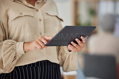 Close up cropped view of a unrecognizable ethnic woman using a tablet while stand in a office at work in a office. Mixed race woman using a wireless device to answer emails at her job.