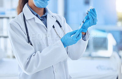 Shot of a female doctor preparing a dose of medication in a syringe while wearing a mask and labcoat inside of a hospital room. Ready to administer an injection of the corona virus vaccine to patients