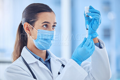 Buy stock photo Young mixed race female doctor wearing a mask while preparing a vaccine at a hospital. Serious hispanic female doctor standing and extracting liquid from a vial with a syringe at a clinic
