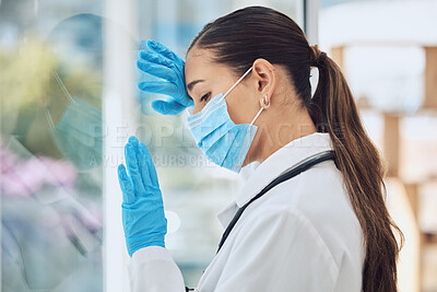 Buy stock photo Young stressed and overworked doctor wearing mask and gloves while standing at a window in a hospital or clinic. One female only looking worried, hopeless and anxious while struggling with a challenge