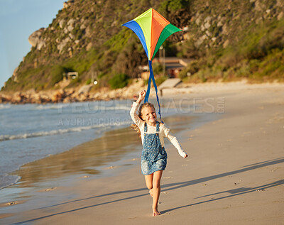 Buy stock photo Portrait of one cute little caucasian girl running alone on the beach sand while holding her kite on a sunny summer day. Young brunette girl smiling and having fun while enjoying a day at the beach and looking free and innocent on a holiday destination