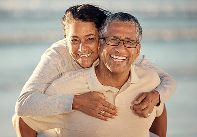 Buy stock photo Closeup portrait of an senior affectionate mixed race couple standing on the beach and smiling during sunset outdoors. Hispanic couple showing love and affection on a romantic date at the beach and husband carry wife of his back