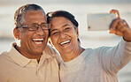 Closeup of an senior affectionate mixed race couple standing on the beach and smiling and taking a selfie with a smartphone during sunset outdoors. Hispanic couple showing love and affection on a romantic date at the beach