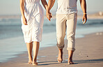 Close up of  mixed race young couple holding hands while walking on the beach together. Hispanic couple traveling and enjoying vacation and being romantic on the beach