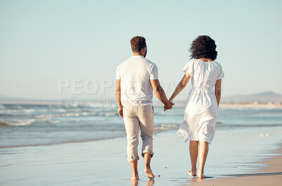 Buy stock photo Rear view of mixed race young couple holding hands while walking on the beach together. Hispanic couple traveling and enjoying vacation and being romantic on the beach