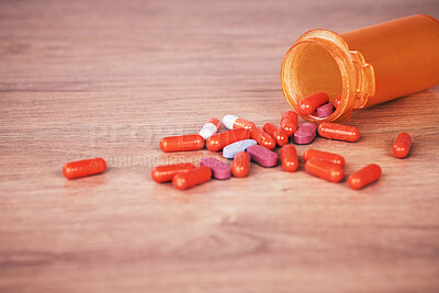 An open orange bottle of brightly coloured pills spilled onto a wooden table. Vitamin supplements are a good way to stay healthy. Chronic or prescription medication is usually covered by medical aid