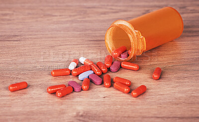 An open orange bottle of brightly coloured pills spilled onto a wooden table. Vitamin supplements are a good way to stay healthy. Chronic and prescription medication is usually covered by medical aid