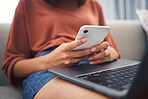 Close up of young female hand's using a smartphone to check messages or send a text on social network while sitting at home with her laptop on her lap