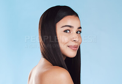 Portrait of one beautiful young hispanic woman with healthy skin and sleek hair smiling against a blue studio background. Happy mixed race model with flawless complexion and natural beauty