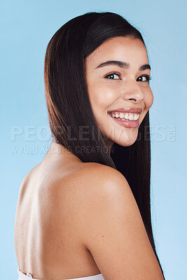 Portrait of one beautiful young hispanic woman with healthy skin and sleek long hair smiling against a blue studio background. Happy mixed race model with flawless complexion and natural beauty