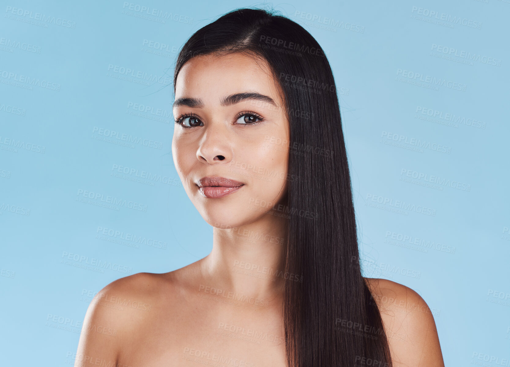 Buy stock photo Portrait of one beautiful young hispanic woman with healthy skin and sleek long hair posing against a blue studio background. Mixed race model with flawless complexion and natural beauty