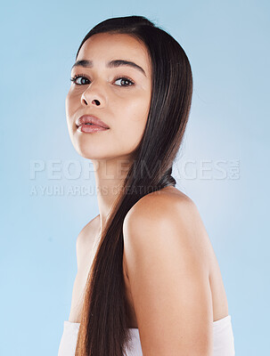 Portrait of one beautiful young hispanic woman with healthy skin and sleek long hair posing against a blue studio background. Mixed race model with flawless complexion and natural beauty