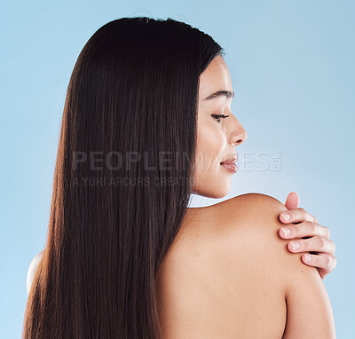 Buy stock photo One beautiful young hispanic woman with healthy skin and sleek long hair looking over and touching shoulder while posing against a blue studio background. Mixed race model with flawless complexion and natural beauty