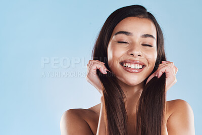 Buy stock photo One beautiful young hispanic woman touching her sleek, silky and healthy long hair while smiling against a blue studio background. Confident and happy mixed race model with flawless complexion and natural beauty