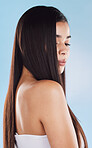 One beautiful young hispanic woman with healthy skin and sleek long hair looking over shoulder while posing against a blue studio background. Mixed race model with flawless complexion and natural beauty