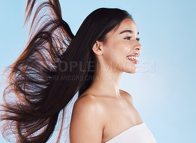 One beautiful young hispanic woman with healthy skin and sleek long hair blowing in the wind smiling against a blue studio background. Happy mixed race supermodel with flawless complexion and natural beauty