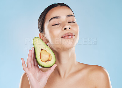 Beautiful young mixed race woman with an avocado isolated in studio against a blue background. Her skincare regime keeps her fresh. For glowing skin, eat healthy. Packed with vitamins and nutrients