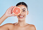Beautiful young mixed race woman with a grapefruit isolated in studio against a blue background. Her skincare regime keeps her fresh. For glowing skin, eat healthy. Packed with vitamins and nutrients