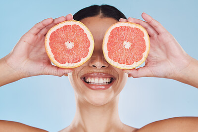 Buy stock photo Grapefruit, woman skincare and face skin with fruit for wellness, health and facial on a blue background in studio. Happy, smile and beauty model with food product in hands hiding eyes with vitamin c
