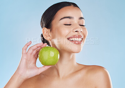 Beautiful young mixed race woman with an apple isolated in studio against a blue background. Her skincare regime keeps her fresh. For glowing skin, eat healthy. Packed with vitamins and nutrients