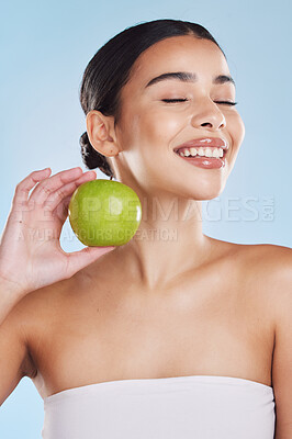 Beautiful young mixed race woman with an apple isolated in studio against a blue background. Her skincare regime keeps her fresh. For glowing skin, eat healthy. Packed with vitamins and nutrients
