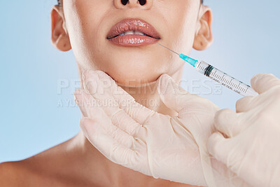 Beautiful young mixed race woman getting plastic surgery botox injection into her lips. Attractive female isolated in studio against a blue background. Modern medicine can enhance your natural beauty