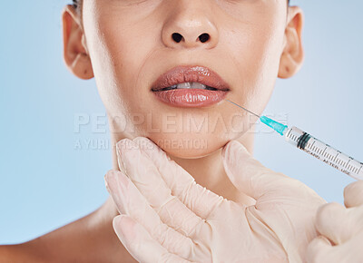 Beautiful young mixed race woman getting plastic surgery botox injection into her lips. Attractive female isolated in studio against a blue background. Modern medicine can enhance your natural beauty