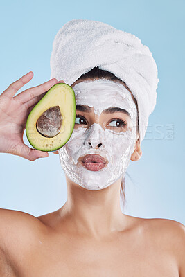 Beautiful young mixed race woman wearing a face mask peel and towel while posing with an avocado. Attractive female clean and fresh out the shower and applying her daily skincare regime to her face
