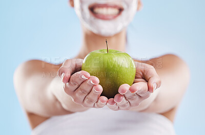 Beautiful young mixed race woman wearing a face mask peel and posing with an apple isolated in studio against a blue background. A skincare regime keeps her fresh. Packed with vitamins and nutrients