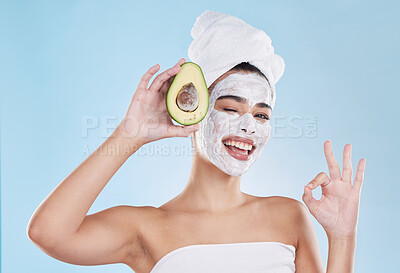 Beautiful young mixed race woman wearing a face mask peel and towel while posing with an avocado. Attractive female clean and fresh out the shower and applying her daily skincare regime to her face
