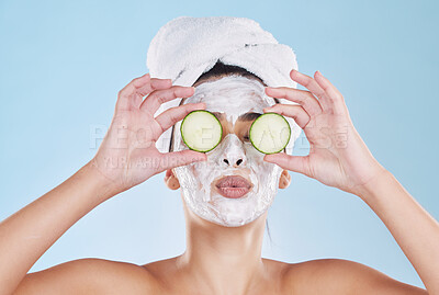 Beautiful young mixed race woman wearing a face mask peel and towel while holding cucumber slices. Attractive female clean and fresh out the shower and applying her daily skincare regime to her face