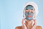 Beautiful young mixed race woman applying a face mask peel isolated in studio against a blue background. Attractive woman with a towel on her head after a shower. Her skincare regime keeps her fresh
