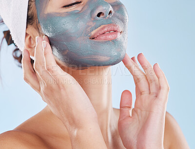 Beautiful young mixed race woman applying a face mask peel isolated in studio against a blue background. Attractive woman with a towel on her head after a shower. Her skincare regime keeps her fresh