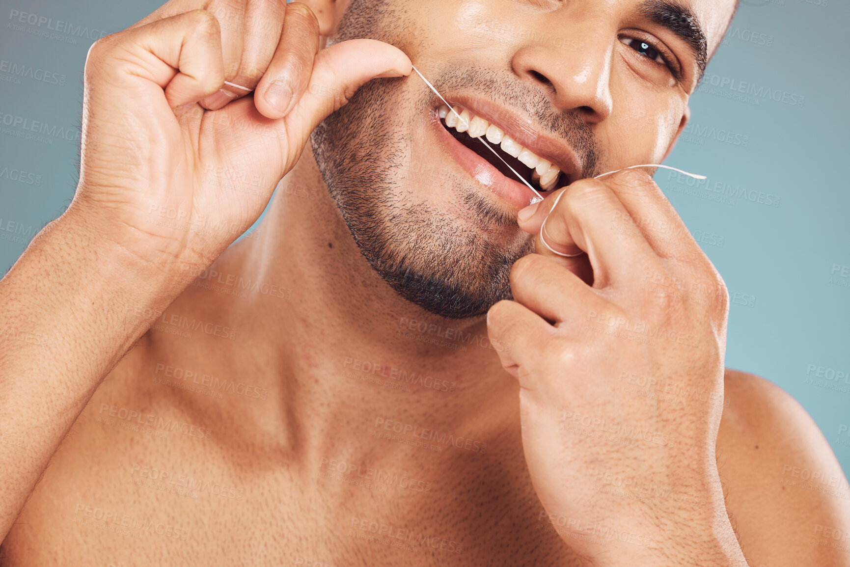 Buy stock photo Closeup of one mixed race man flossing his teeth against a blue studio background. Guy grooming and cleaning his mouth for better oral and dental hygiene. Floss daily to prevent tooth decay and gum disease