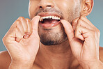 Closeup of one mixed race man flossing his teeth against a blue studio background. Guy grooming and cleaning his mouth for better oral and dental hygiene. Floss daily to prevent tooth decay and gum disease