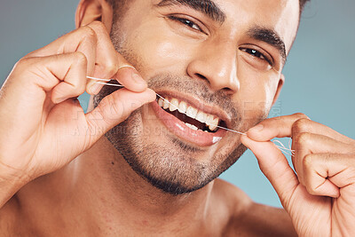Buy stock photo Portrait of one smiling young indian man flossing his teeth against a blue studio background. Handsome guy grooming and cleaning his mouth for better oral and dental hygiene. Floss daily to prevent tooth decay and gum disease