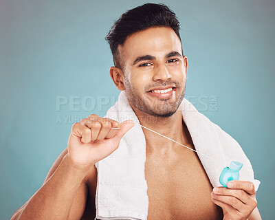 Buy stock photo Portrait of one smiling young indian man with towel around neck flossing his teeth after a shower against a blue studio background. Happy guy cleaning his mouth for better oral and dental hygiene. Floss daily to prevent tooth decay and gum disease