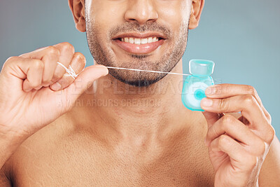 Buy stock photo Closeup of one smiling mixed race man flossing his teeth against a blue studio background. Guy holding container of floss for better oral and dental hygiene. Floss daily to prevent tooth decay and gum disease