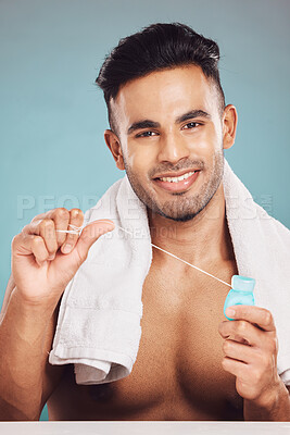 Buy stock photo Portrait of one smiling young indian man with towel around neck flossing his teeth after a shower against a blue studio background. Happy guy cleaning his mouth for better oral and dental hygiene. Floss daily to prevent tooth decay and gum disease
