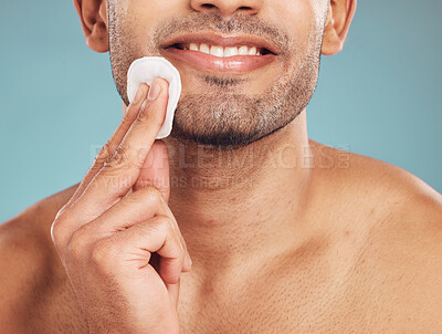 Buy stock photo Closeup of one mixed race man wiping a round cotton swab on his face while grooming against a blue studio background. Handsome guy cleaning and exfoliating his face for a healthy complexion and clear skin