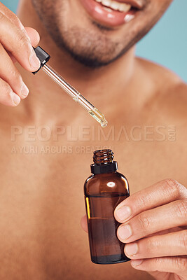 Buy stock photo Closeup of one mixed race man using a dropper to apply serum oil from a bottle to his skin and face against a blue studio background. Guy holding a moisturising aftershave product for healthy, smooth and soft skin